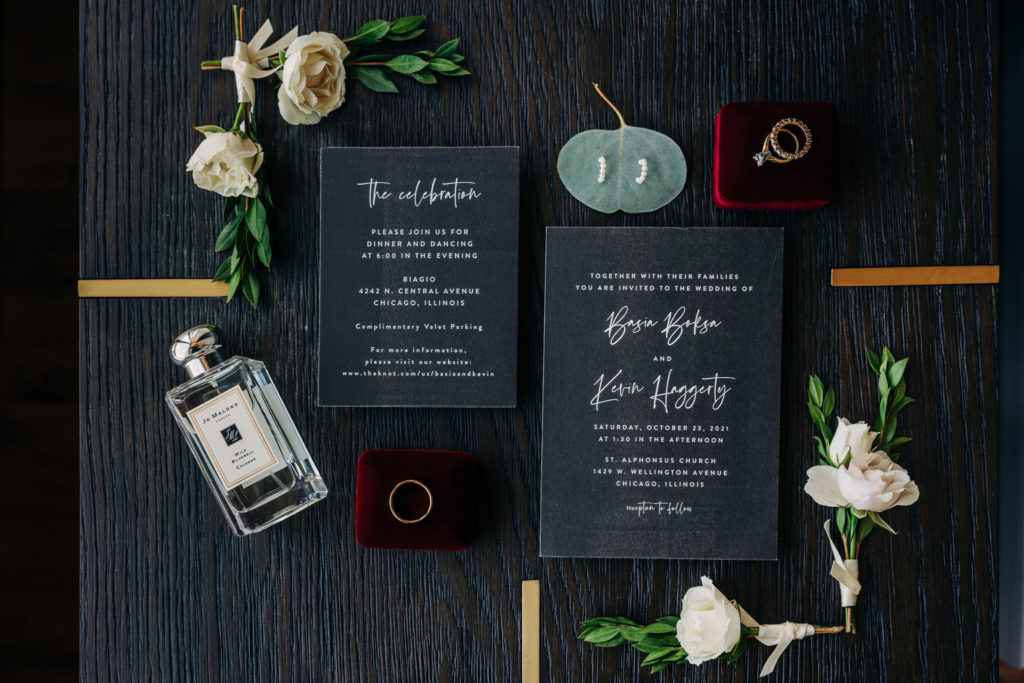 A flat-lay of the bride and groom's important objects for the day, including their rings, invitations, and the bride's earrings and perfume.