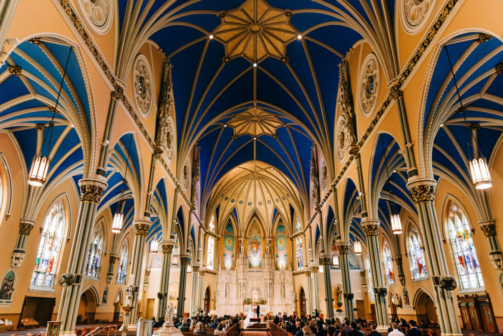 The blue and gold vaulted ceiling of St. Alphonsus church, with the bride and groom standing at the altar in the distance.