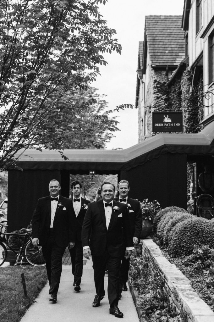 The groomsmen walking together in front of the ivy-covered Deer Path Inn