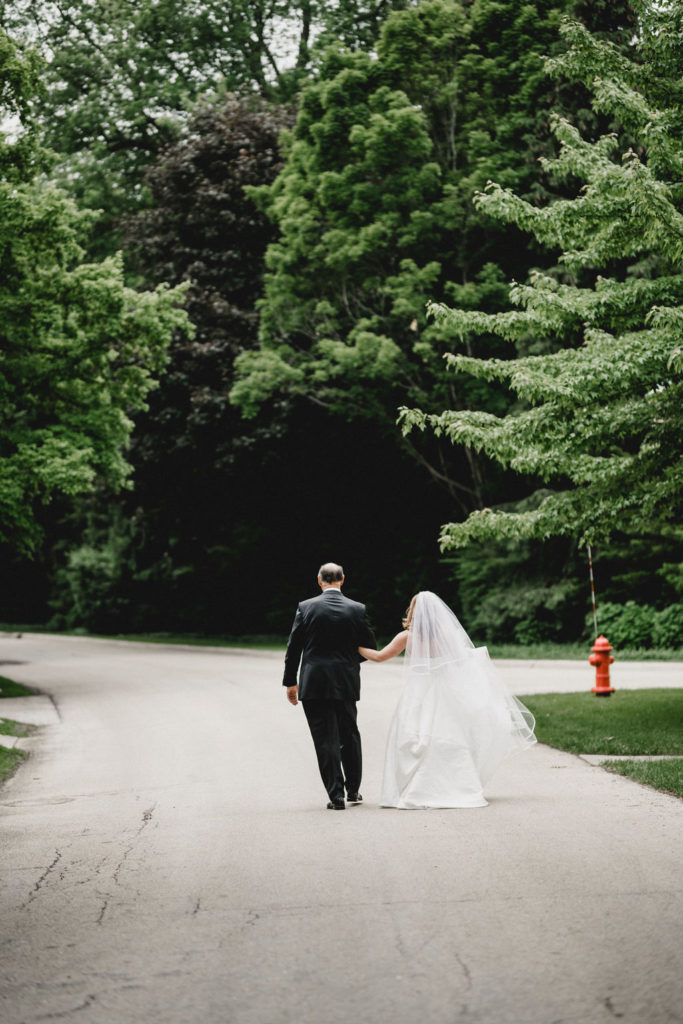 The bride and her father walk down a tree-lined street to church